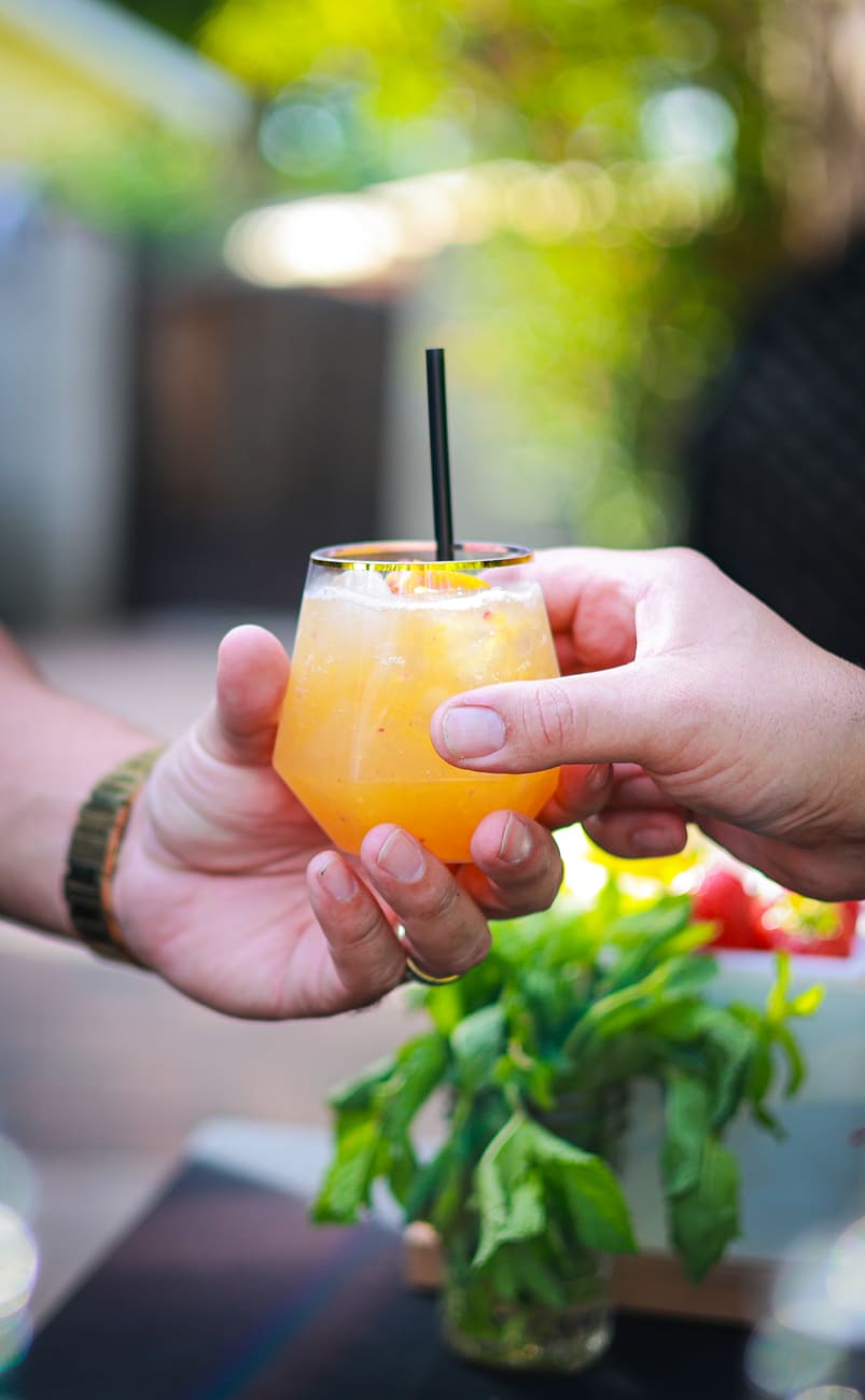 An orange cocktail being handed to a guest across the bar